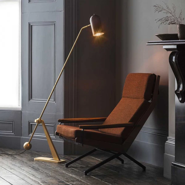 Die Stehleuchte 'Stasis' von Bert Frank steht neben einem rostbraunen Sessel in der Ecke eines dunkelgrauen Zimmers.