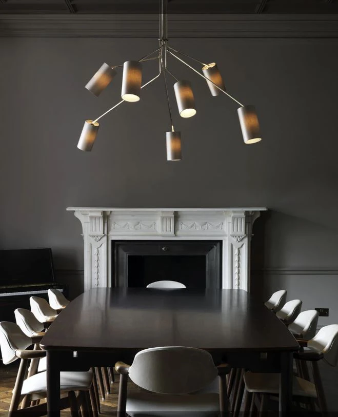 Ein siebenarmiger Leuchter von CTO Lighting hängt über einem Esstisch mit zehn Stühlen in einem dunklen Raum.