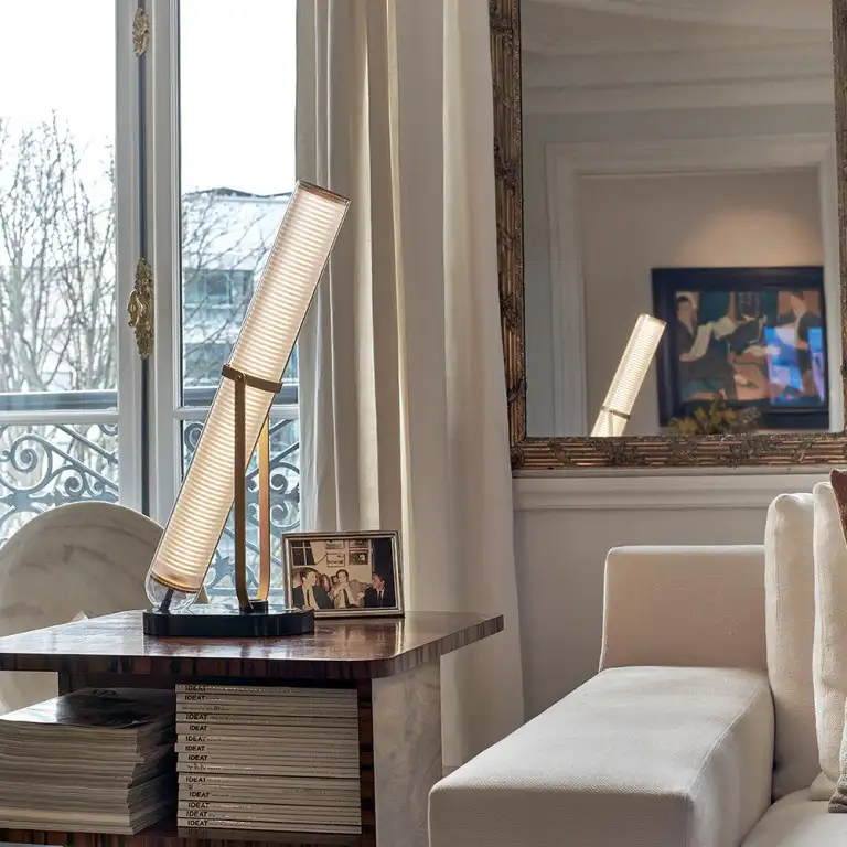 Ein helles Wohnzimmer mit goldgerahmtem Spiegel, auf einem Tisch steht die Leuchte 'Frechin' von DCW éditions