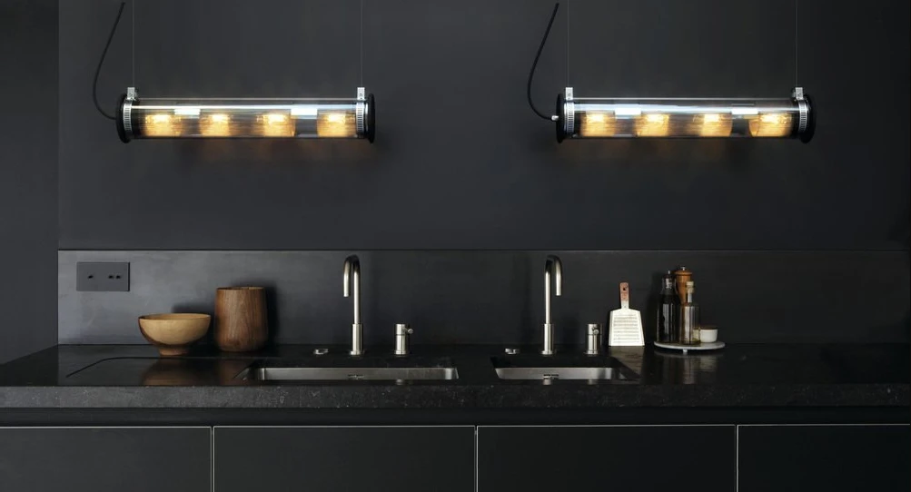 Eine schwarze Küchenspüle mit schwarzer Rückwand, darüber zwei Leuchten 'Tube' von DCW Lighting.