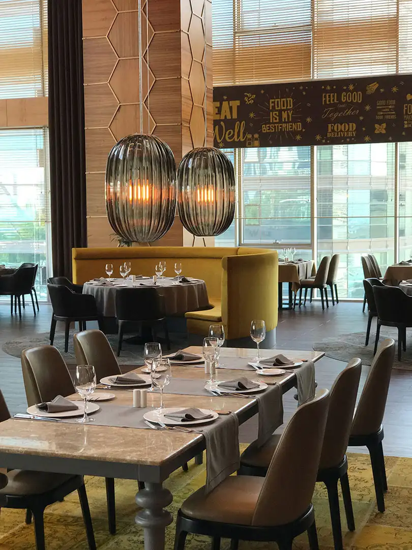 Man sieht in ein Restaurant mit mehreren Tischen, im Vordergrund ein Tisch mit sechs Stühlen, darüber hängen zwei Leuchter 'Plass' von Foscarini aus grauem Glas.