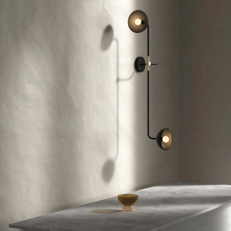 Die filigrane schwarze zweiarmige Wandleucht 'Beaubien' hängt an einer hellen Wand über einem Marmortisch, auf dem eine kleine Kelch-Schale steht.