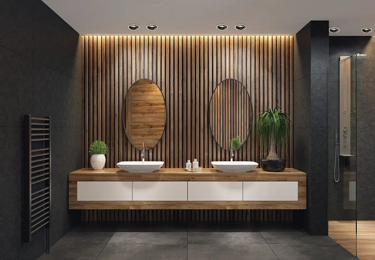 Ein Badezimmer mit dunklen Wänden und einer Holzverkleidung hinter den Waschbecken, über denen zwei ovale Spigel hängen.
