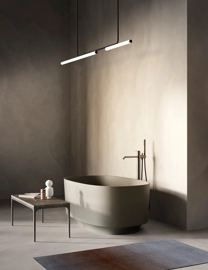Eine röhrenförmige Leuchte von Marset hängt über einer modernen Badewanne in Grau.