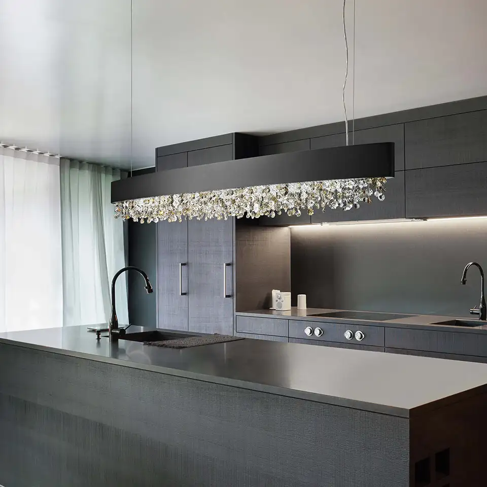 Über der Arbeitsfläche einer dunkelgrauen Küche hängt ein ellipsenförmiger großer Leuchter mit vielen kleinen Glaselementen.