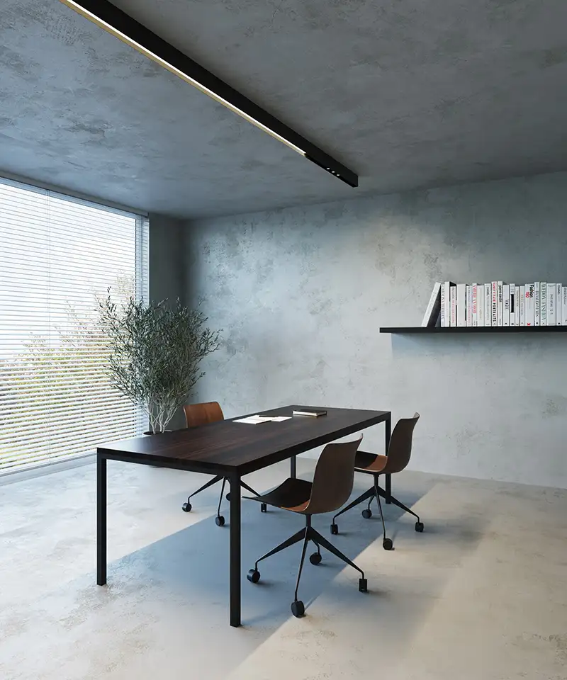 Ein puristisches Arbeitszimmer mit Wänden und Decke in Betonoptik, in der Mitte ein Schreibtisch mit drei Stühlen.
