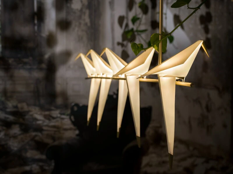 Fünf wie aus Papier gefaltete Vögel sitzen hintereinander auf einer Stange und bilden die Leuchte 'Perch Light' von Moooi