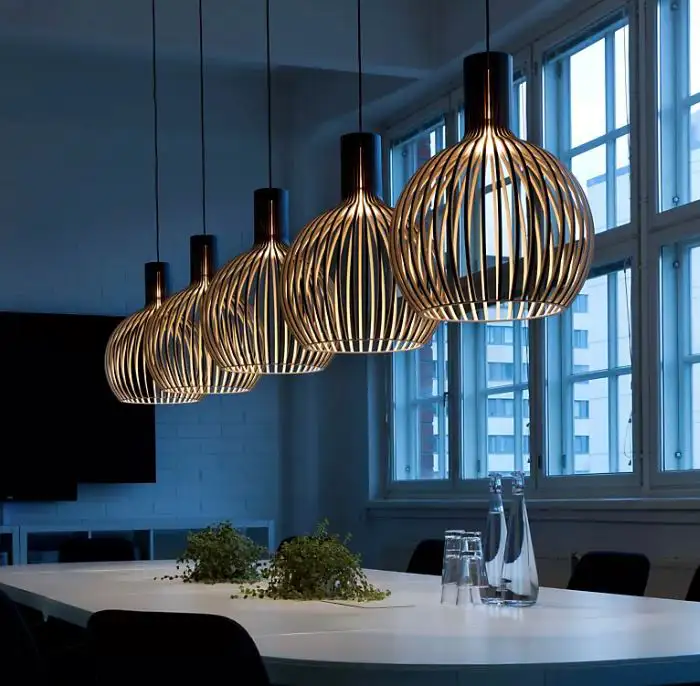 Fünf Leuchter 'Octo' von Sectodesign aus kugelförmig gebogenen Holzleisten hängen hintereinander über einem Esstisch.