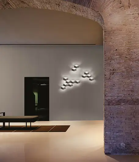 Durch einen großen gemauerten Rundbogen sieht man auf eine Wand, an der Leuchten aus der 'Fold'-Serie von Vibia hängen