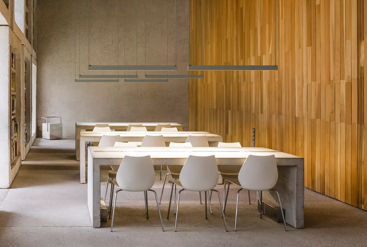 Ein Speisesaal mit holzvertäfelter Wand, vor der mehrere Tische hintereinander stehen. Darüber hängen jeweils zwei lange schmale Leuchten 'plus-minus' von Vibia.