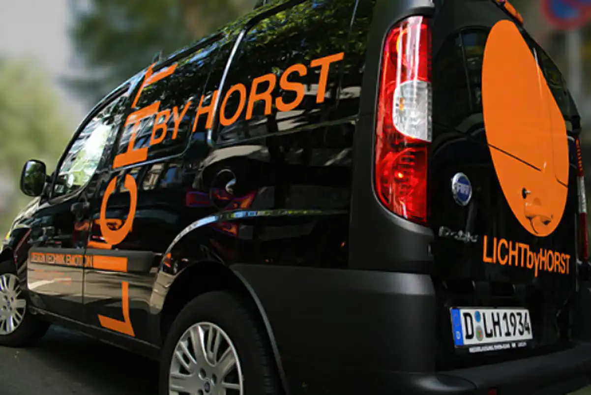 ein schwarzer Lieferwagen mit orangefarbener Beschriftung der Firma Licht by Horst