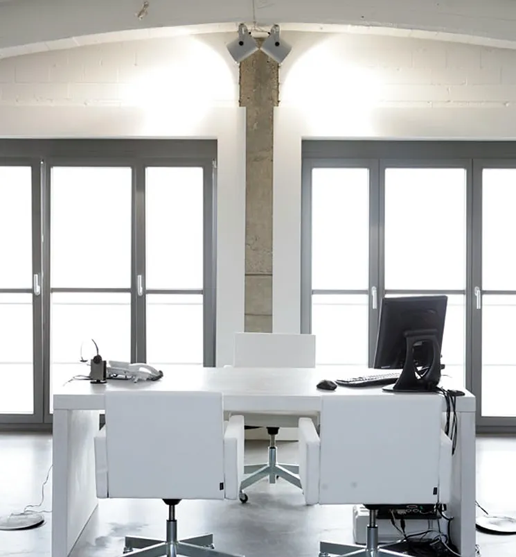 Ein weißer Schreibtisch mit drei weißen Sesseln steht vor einer Fensterfront in einem Loft