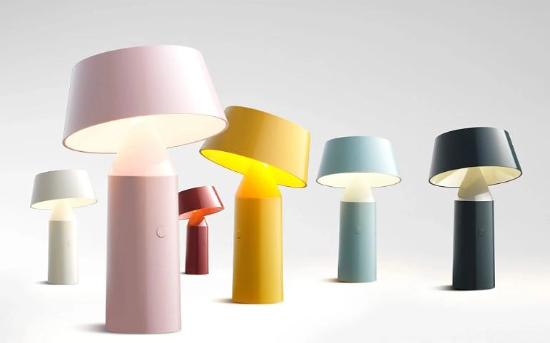 sechs Tischlampen 'Marset Biocca' in unterschiedlichen Farben stehen lose aufgereiht auf einer weißen Fläche