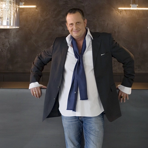 Michael Horst trägt ein dunkles Sakko über einem weißen Hemd, dazu einen locker geknoteten blauen Schal und eine Jeans.